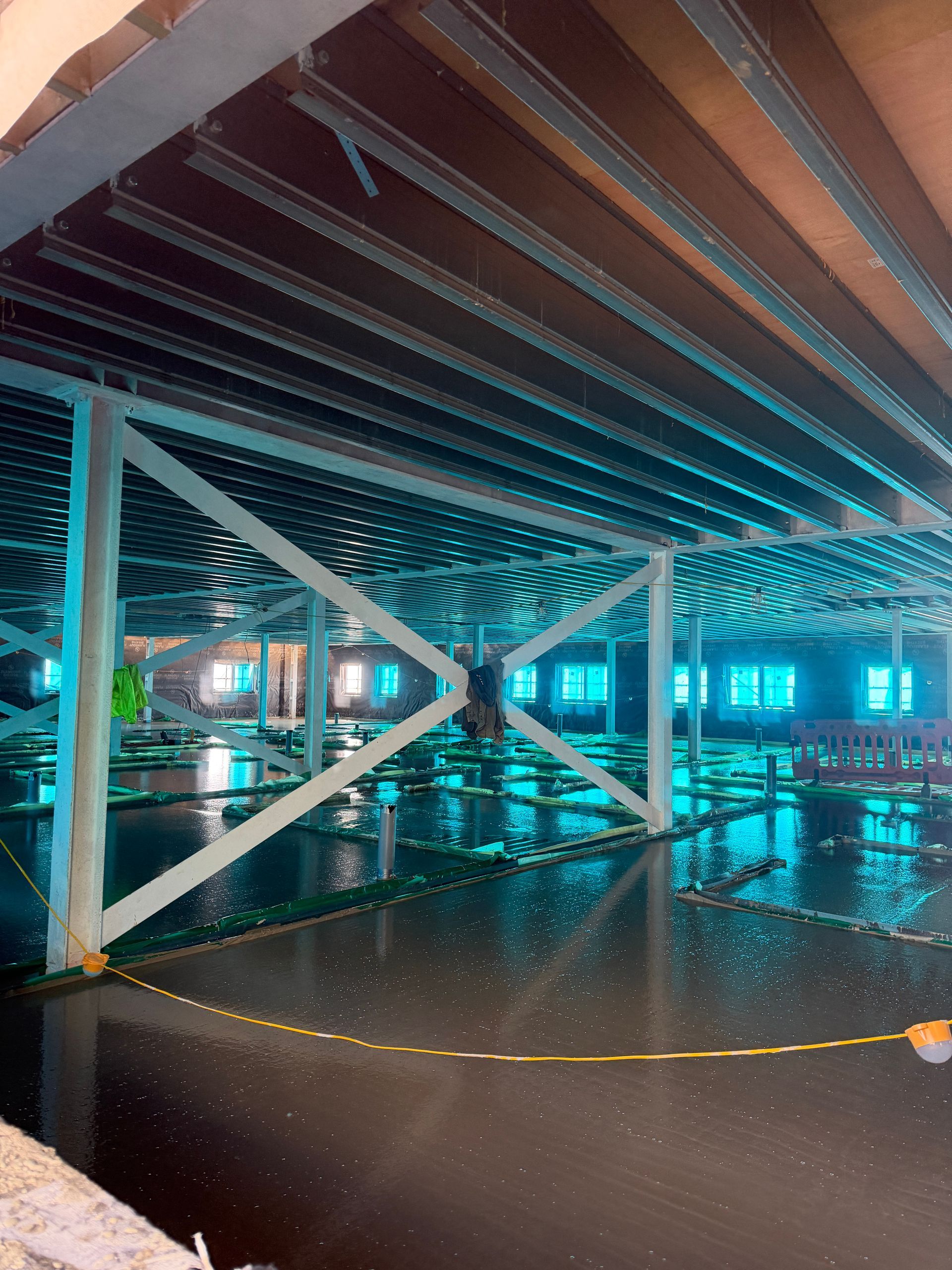 Underground parking garage with blue lighting, metal support beams, and a wet floor reflecting lights.