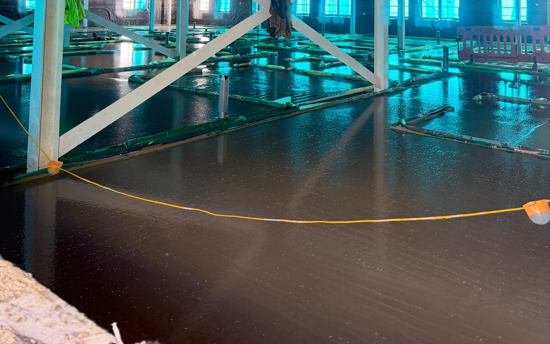 Underground parking garage with blue lighting, metal support beams, and a wet floor reflecting lights.