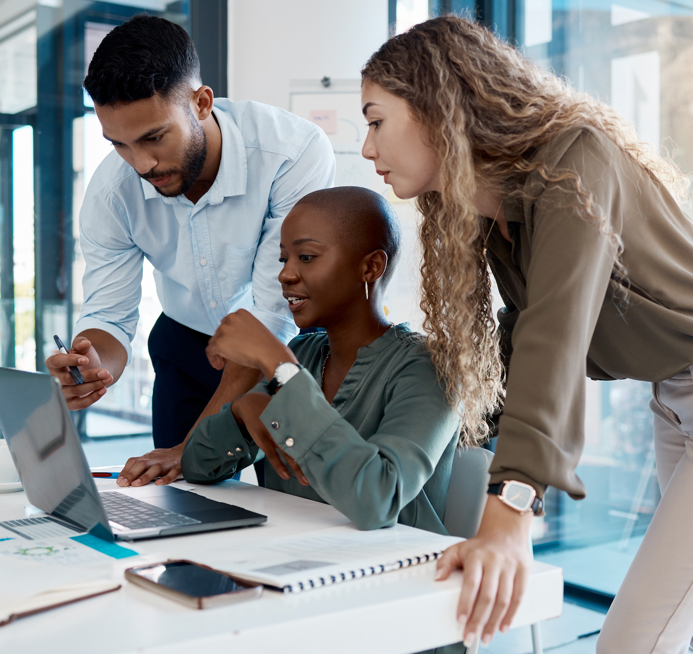 Three business colleagues collaborating around a laptop in an office setting.