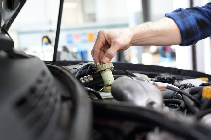 Mano che apre il tappo del serbatoio del liquido del motore di un'auto.
