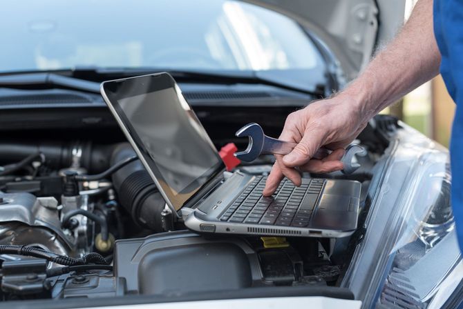 Meccanico che usa un computer portatile per diagnosticare il motore di un'auto con una chiave inglese in mano.