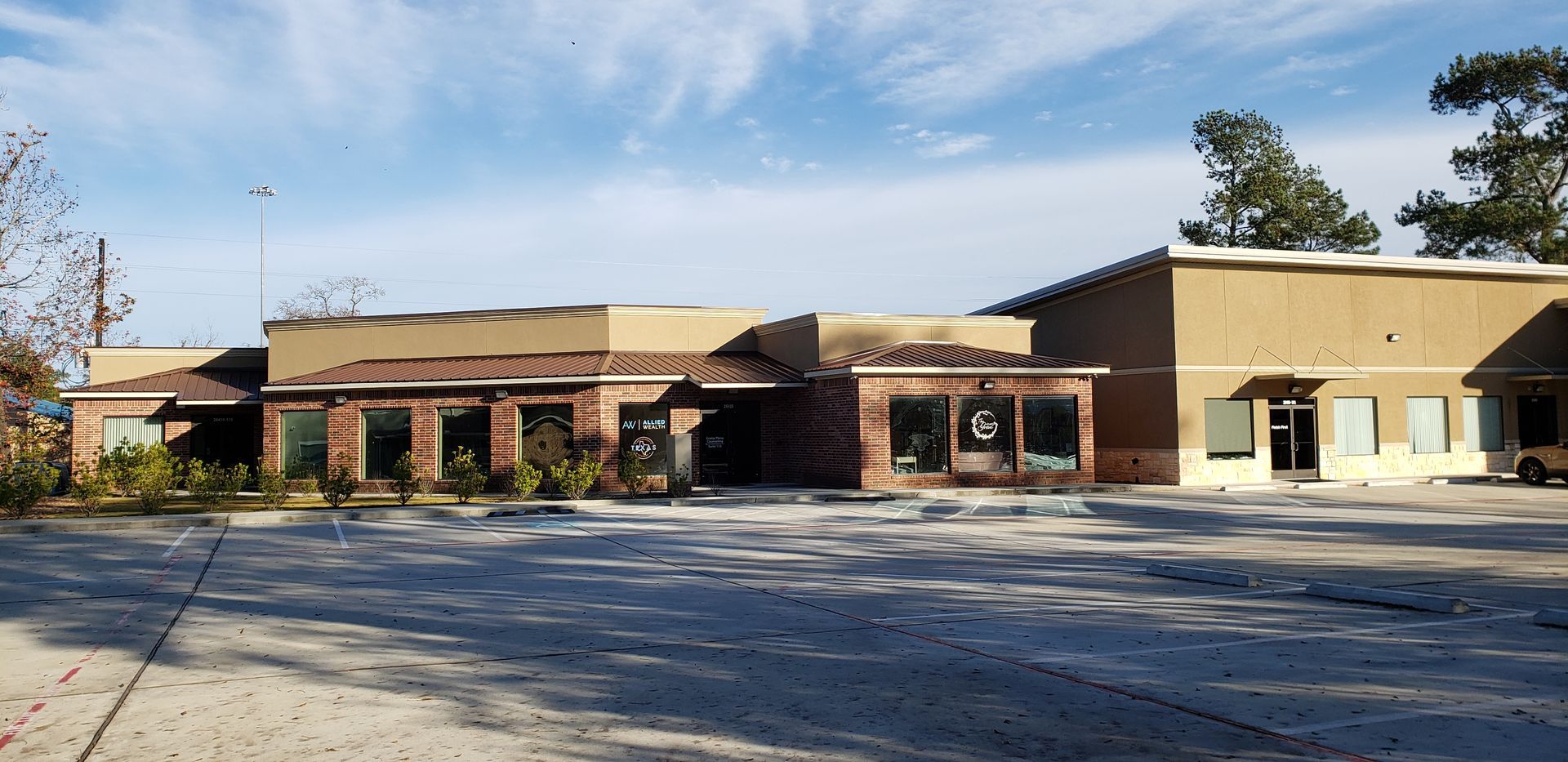 Low brick school building with tan roof and empty parking lot under a blue sky