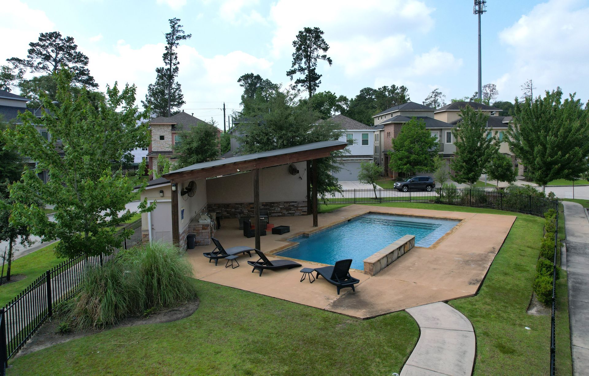 Backyard pool with patio, lounge chairs, and a covered seating area surrounded by green lawn and trees