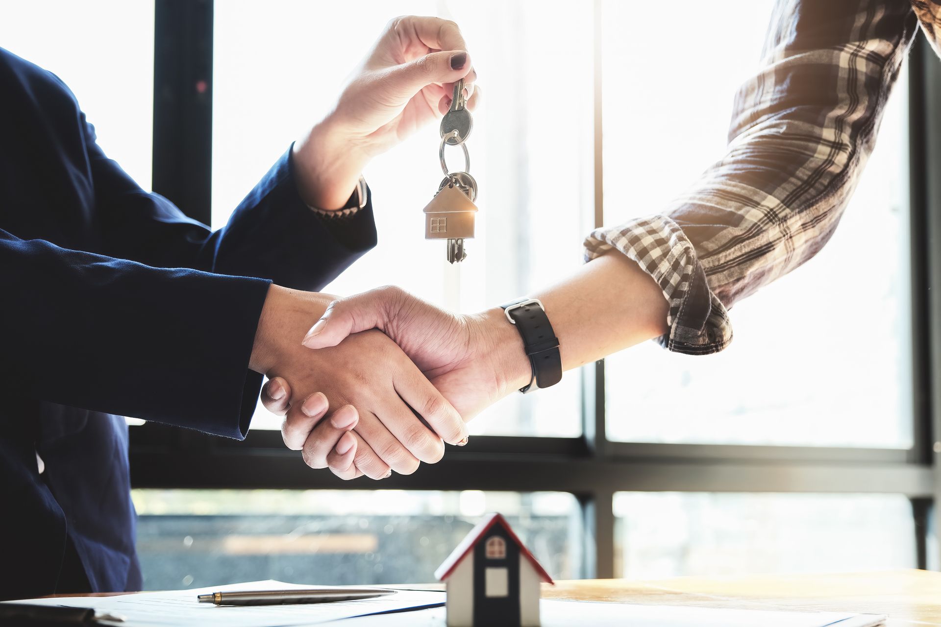 Handshake during a real estate deal with a house model and keys on a desk