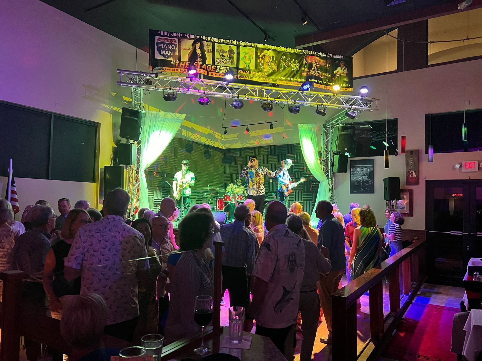 Band performing on a stage lit with colorful lights; audience watches and dances in a club.