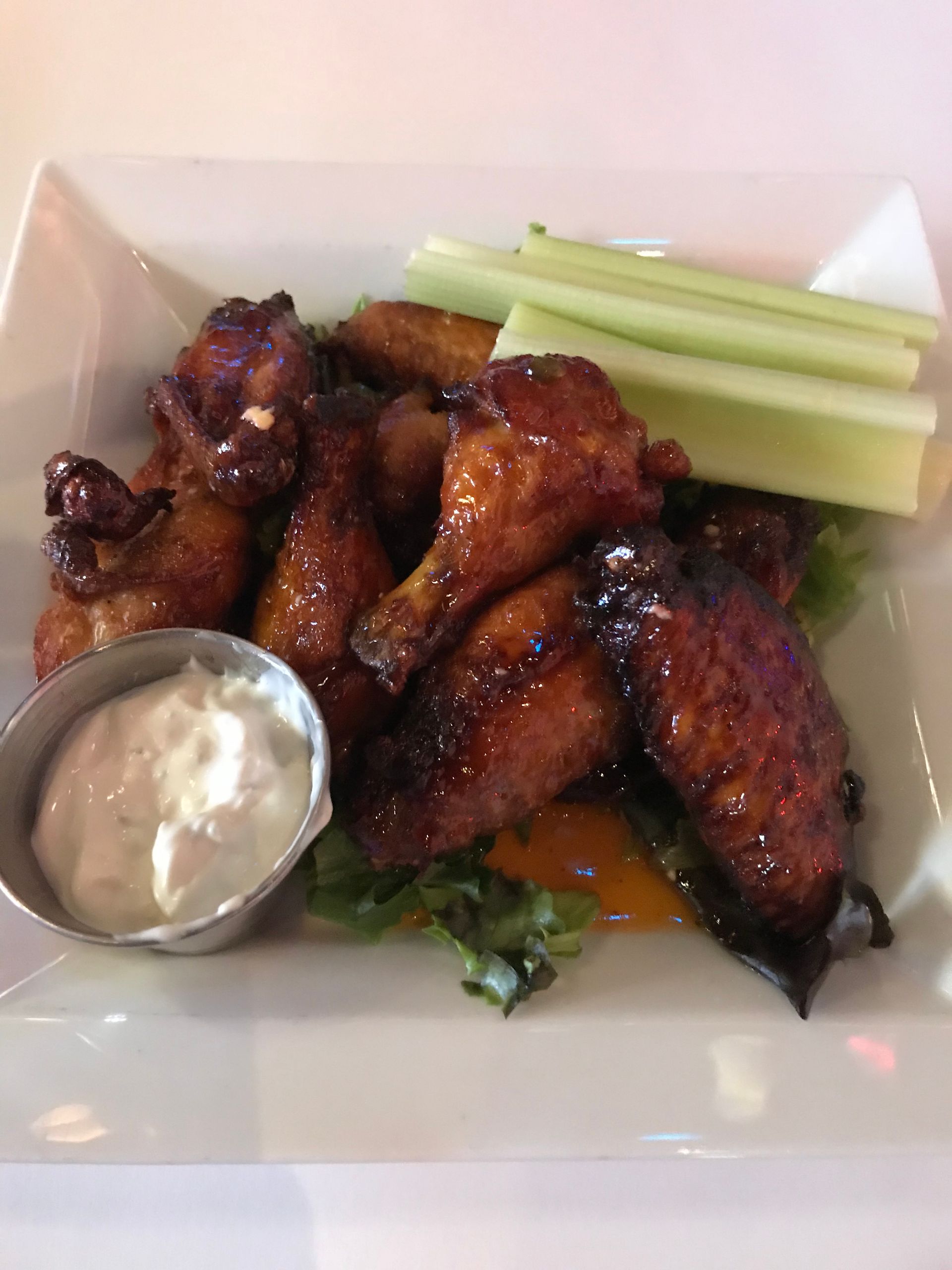Chicken wings with dipping sauce and celery on a white plate.