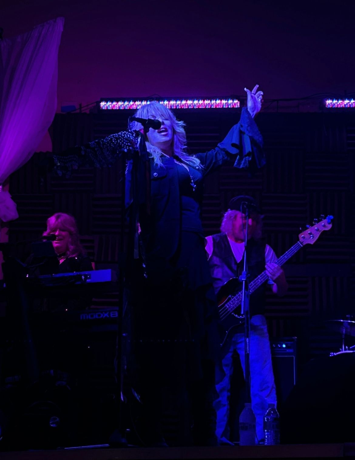 Singer and band onstage under purple lighting, with a keyboardist and guitarist in the background