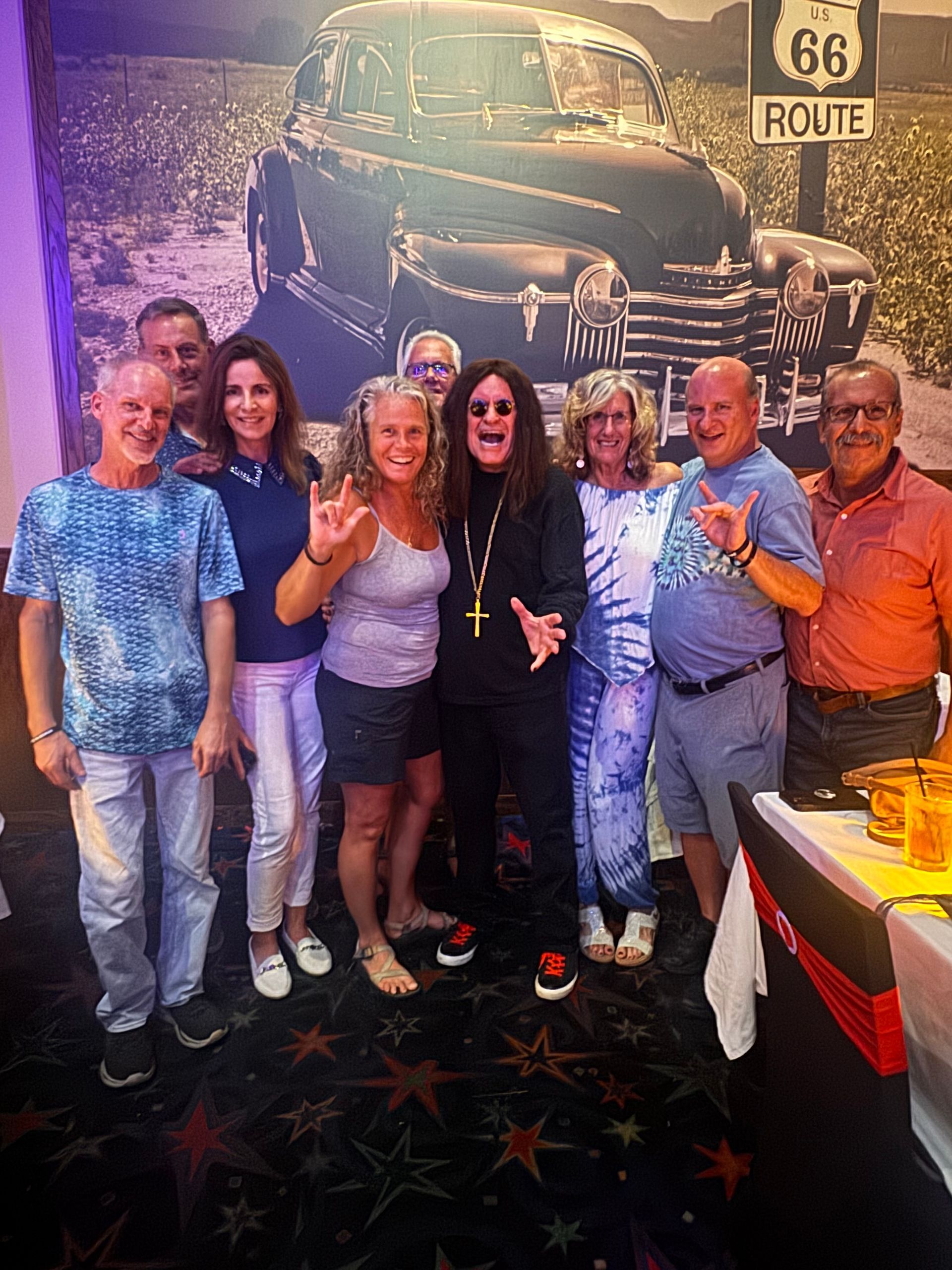 Group of six smiling people posing indoors beside a Route 66 wall mural and truck artwork