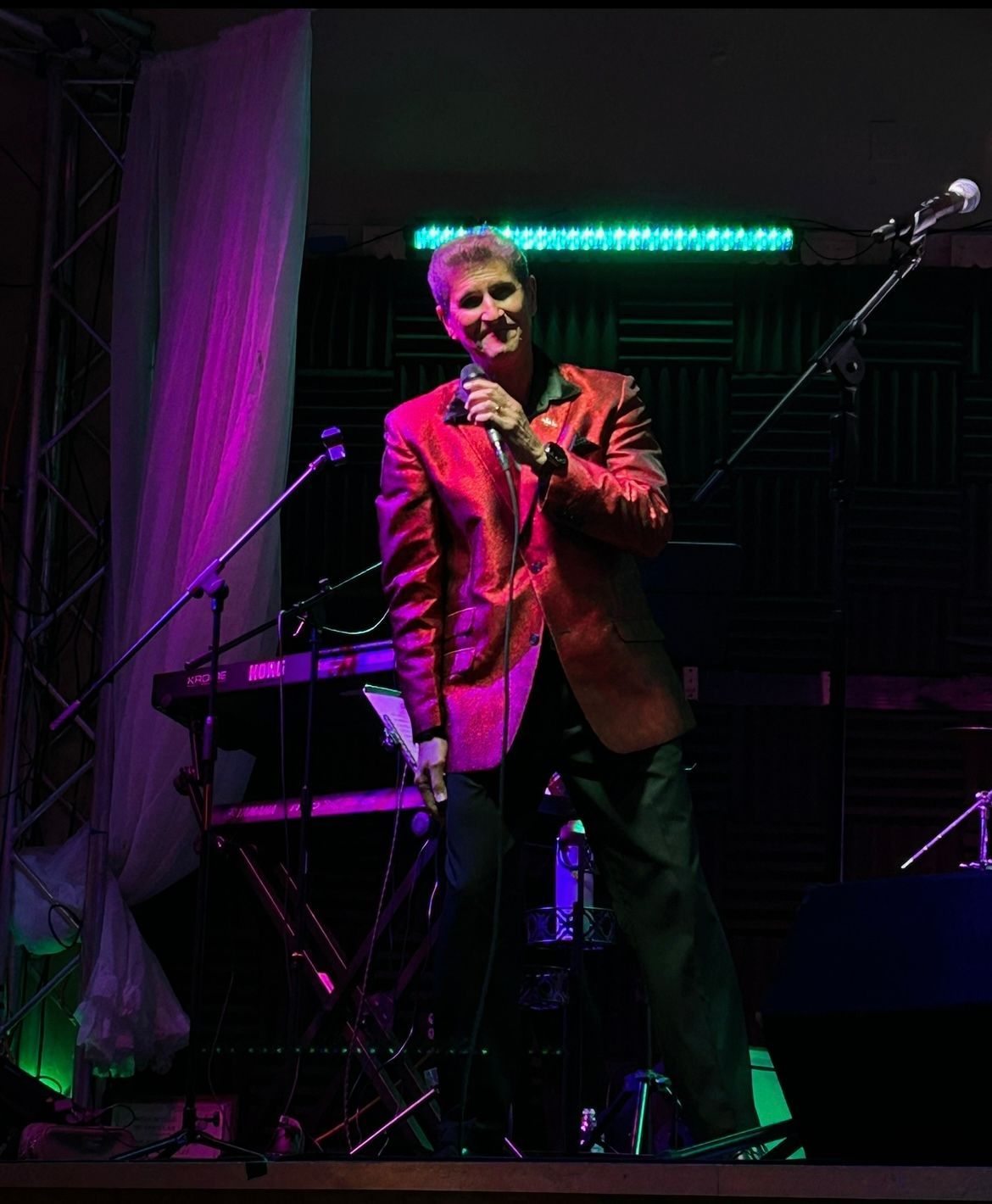 Singer in red blazer performing on stage with a microphone under purple and green lights