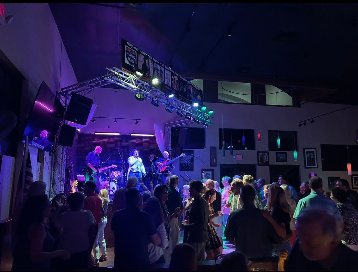 Crowded indoor concert with purple stage lights and a band performing on stage