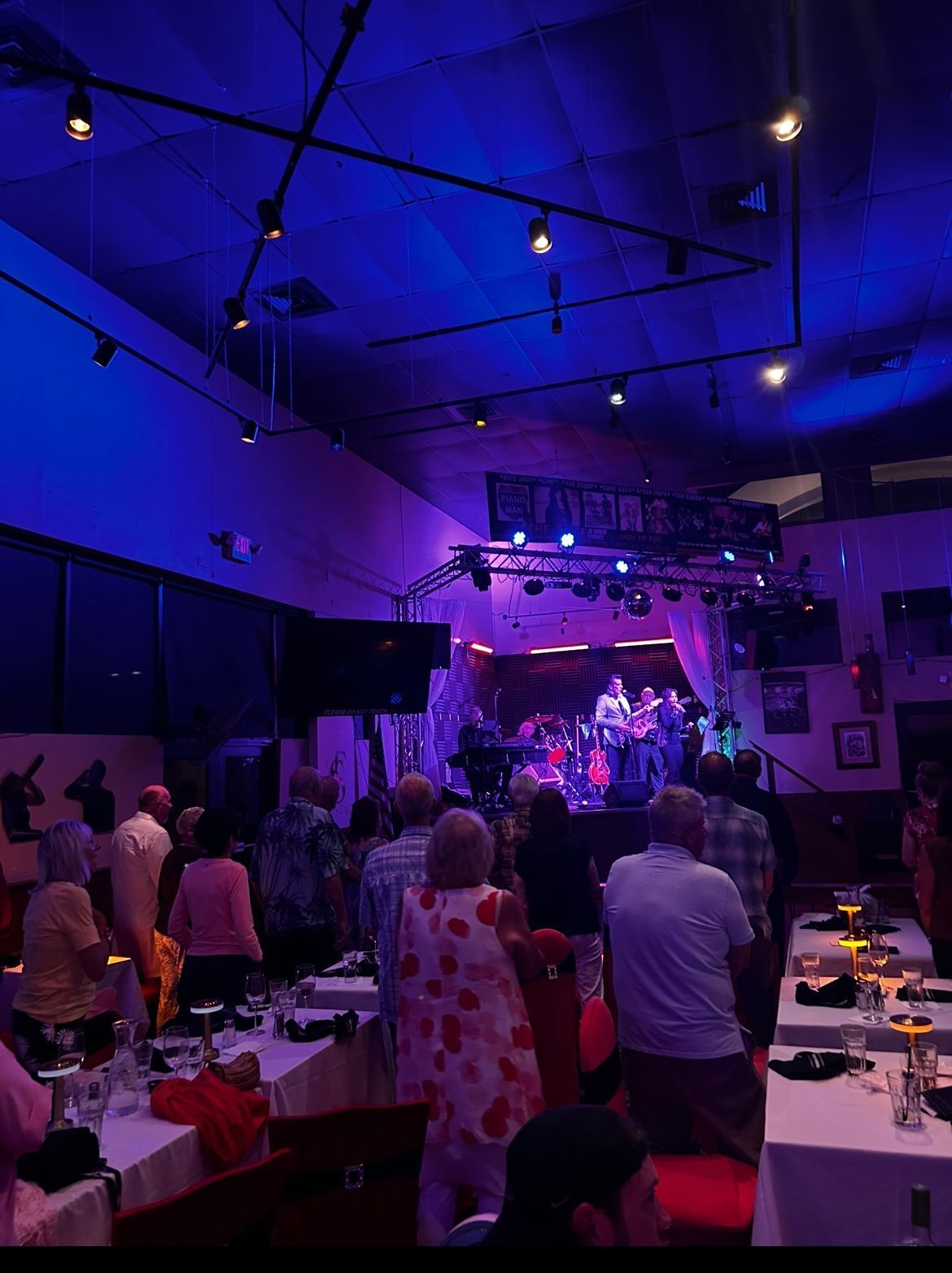 Crowded indoor concert venue with blue-purple lighting and a stage in the distance