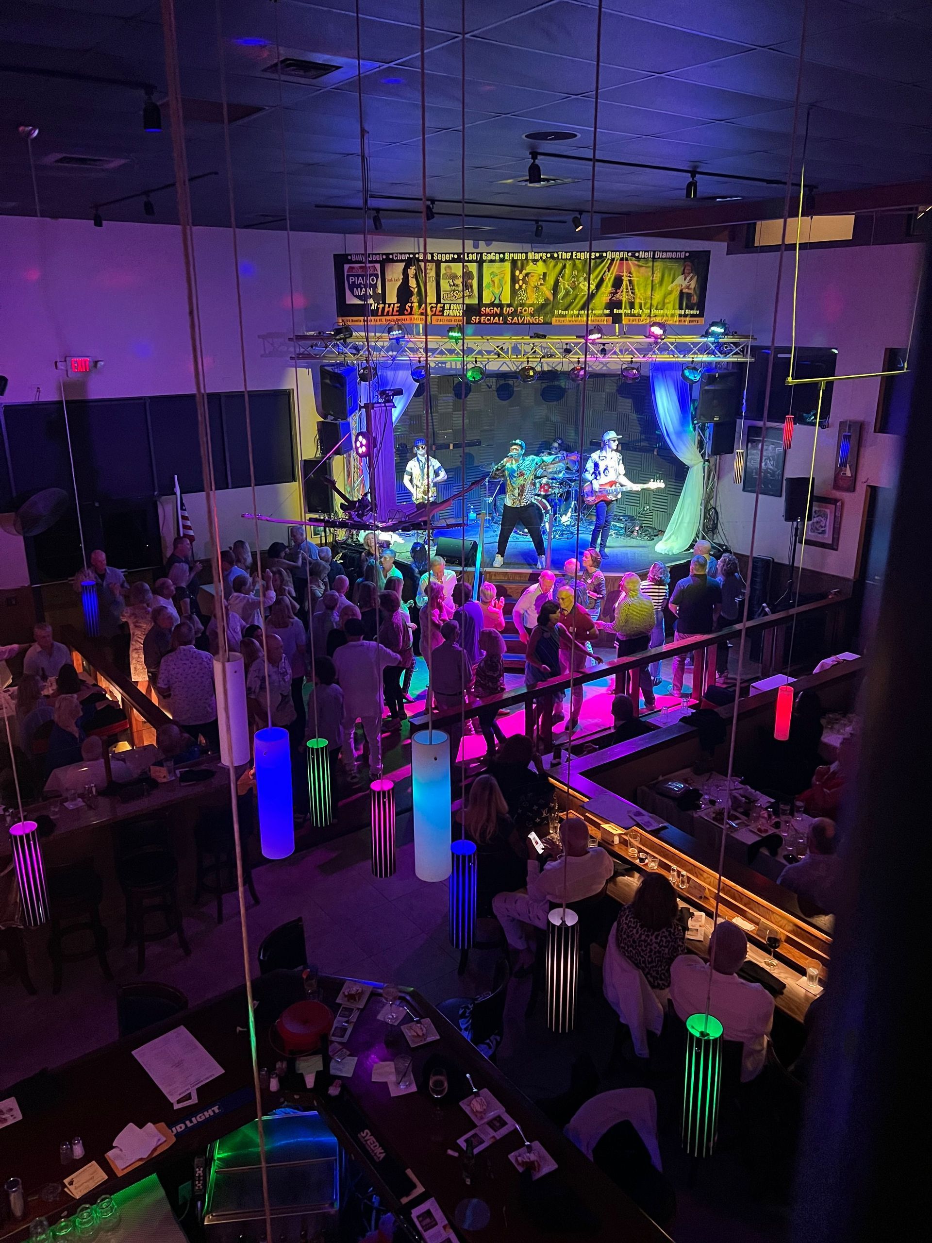 Live music venue with band performing on stage, crowd dancing, colorful stage lights.