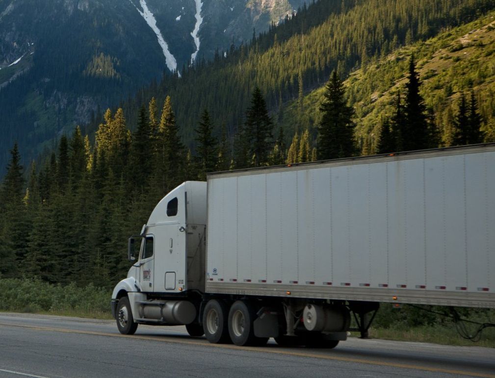 A semi truck is driving down a highway with mountains in the background.
