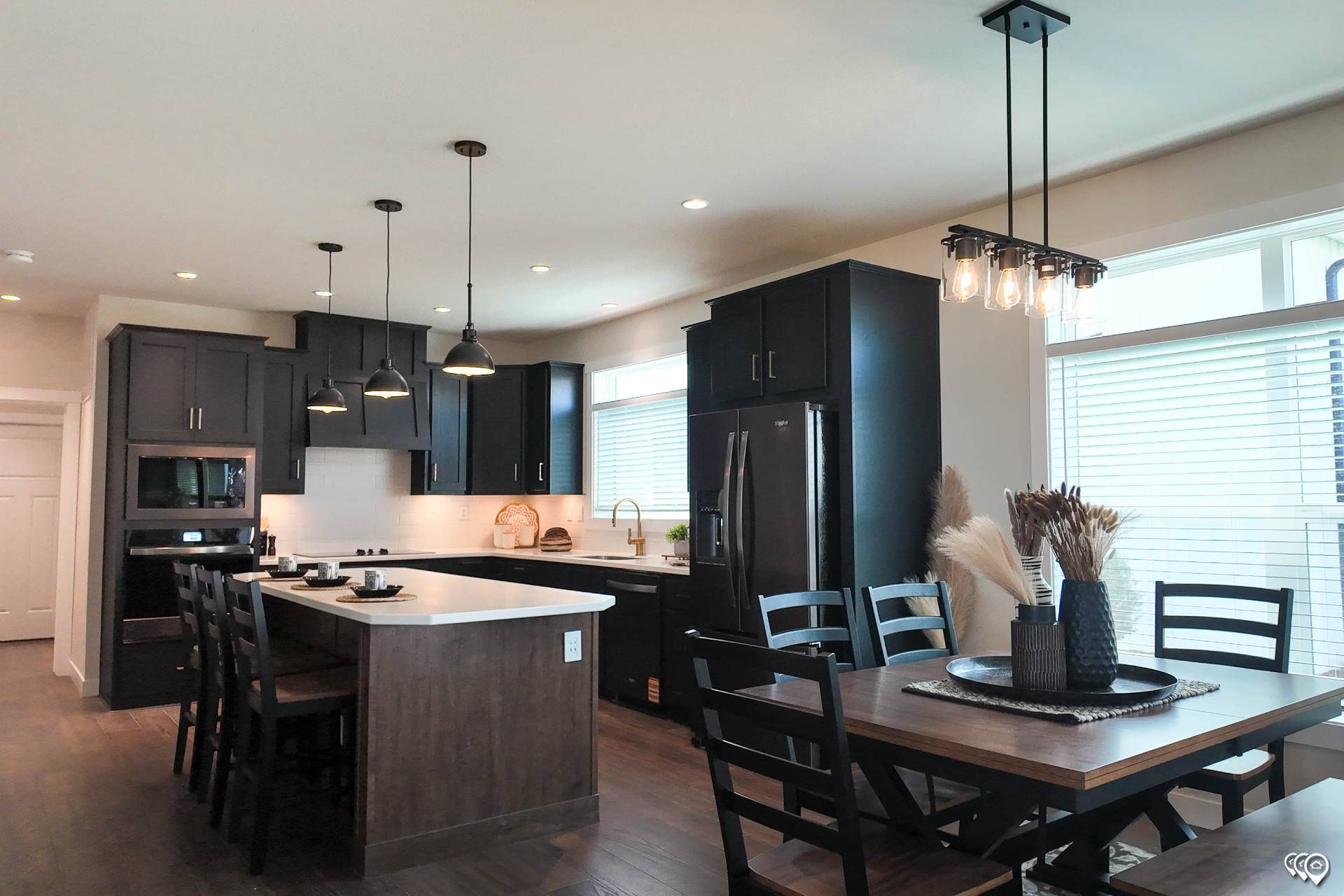 Modern kitchen with dark cabinetry, white countertops, and a dining table.