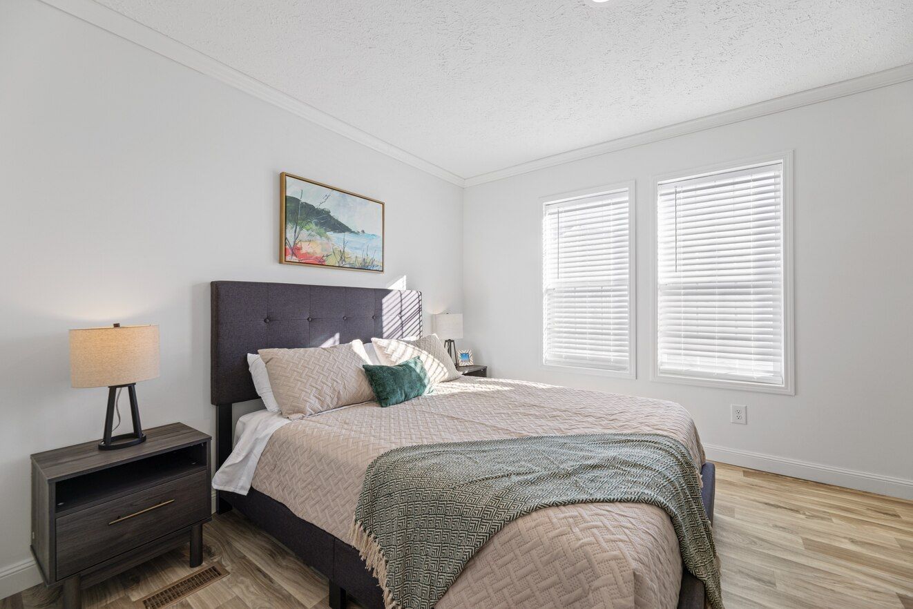 Bedroom with bed, nightstand, lamps, artwork, and windows.