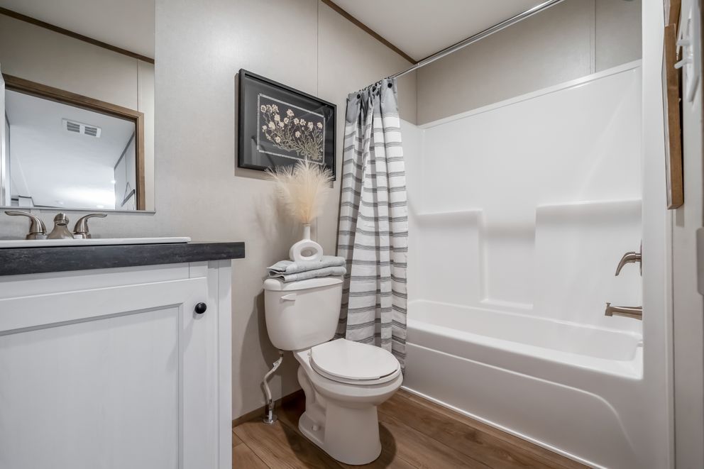 Bathroom with white walls, tub, toilet, vanity, and shower curtain.