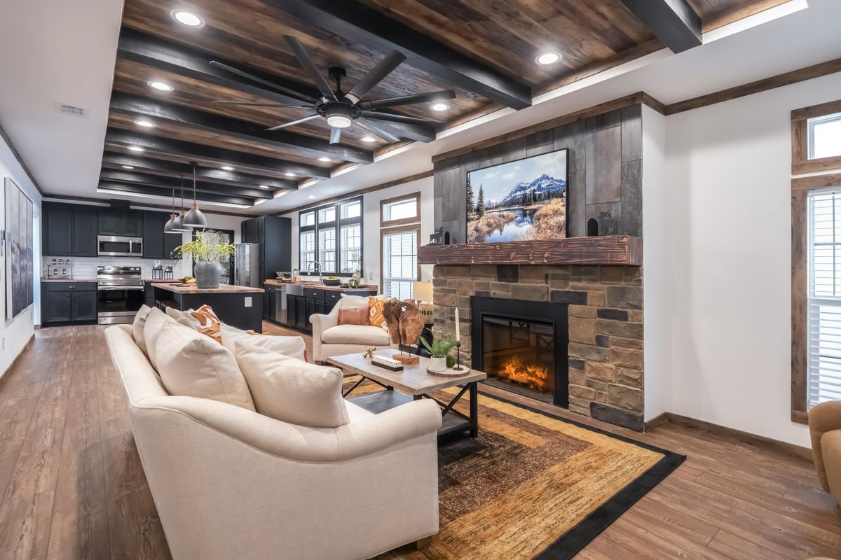 Cozy living room with fireplace, TV, and open-plan kitchen, featuring wood ceiling and flooring.