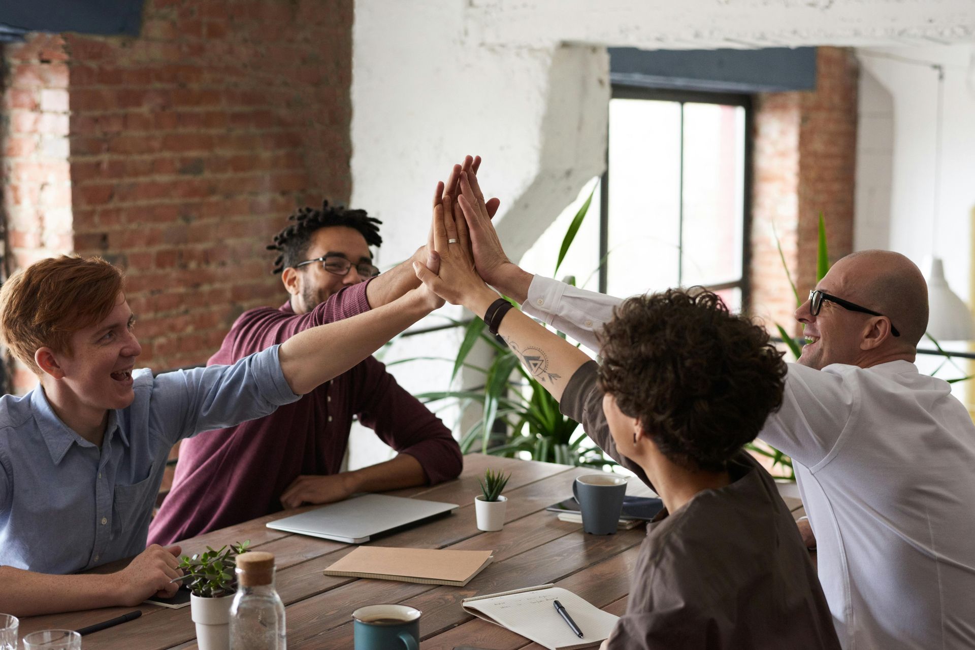 Team of four high-fiving over a wooden table, celebrating a success.