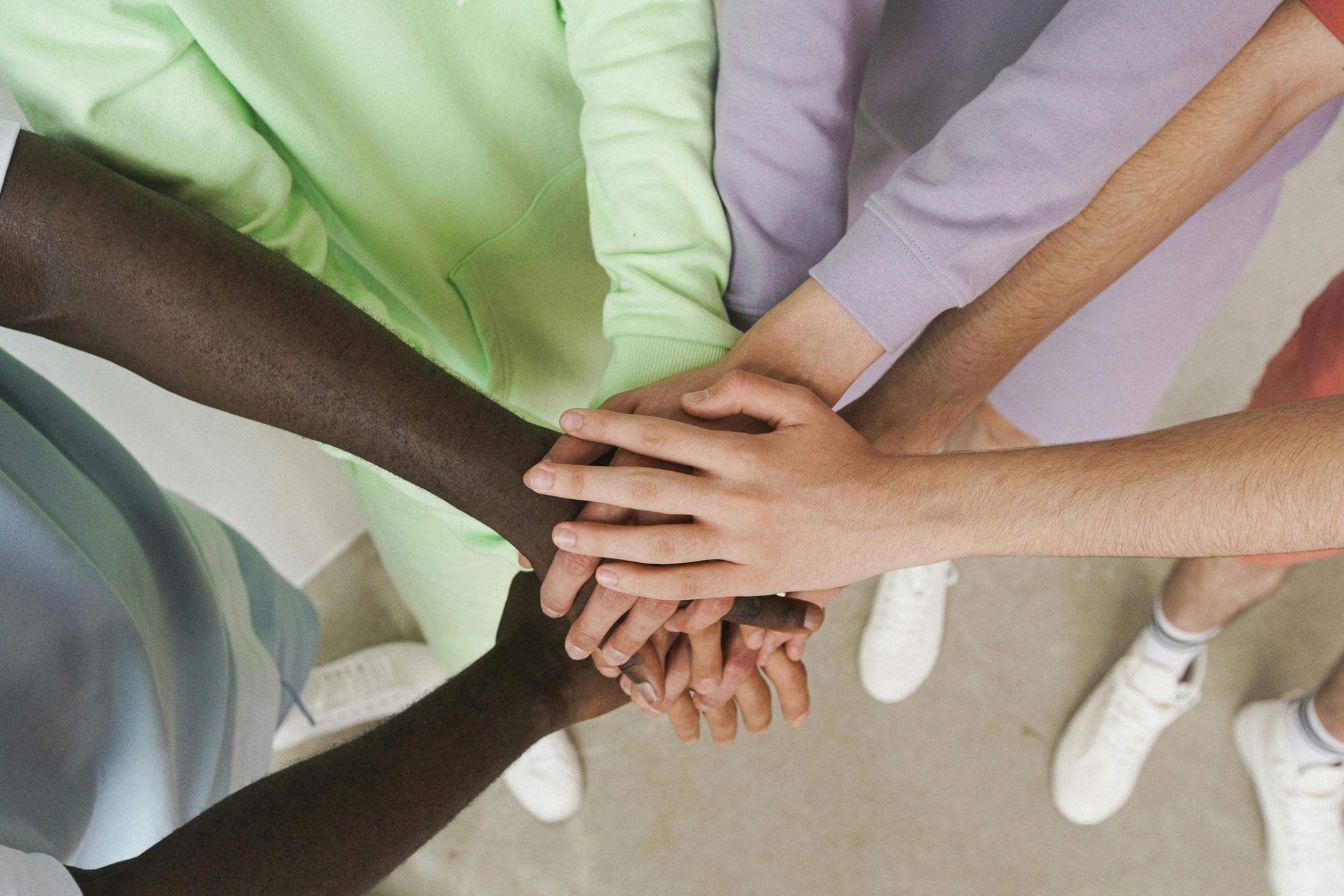 Hands stacked in a group huddle, diverse skin tones, emphasizing teamwork and unity.