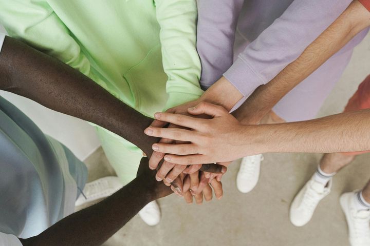 Hands stacked in a group huddle, diverse skin tones, emphasizing teamwork and unity.