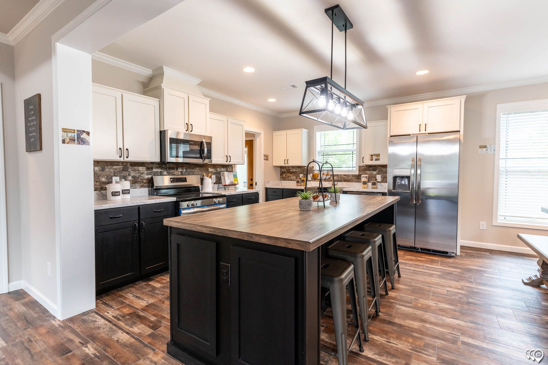 Modern kitchen with black and white cabinets, large island with stools, stainless steel appliances, and wood floors.