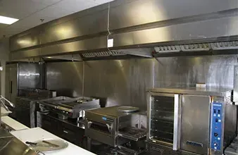 Stainless steel commercial kitchen with ovens, grills, and overhead ventilation hood