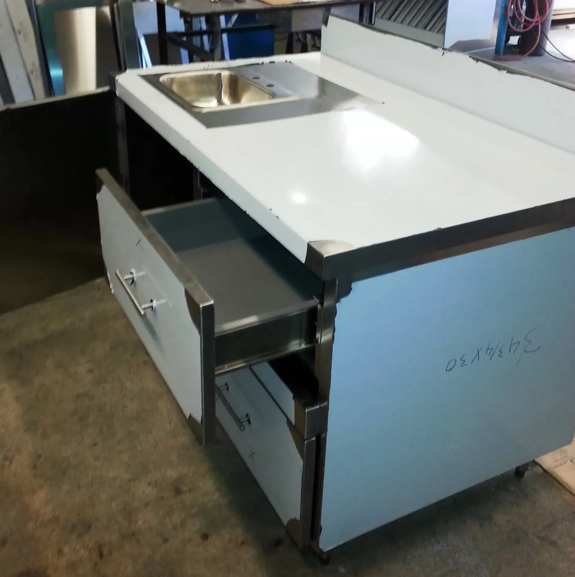 Stainless steel prep island with sink and open drawers in a workshop or kitchen setting