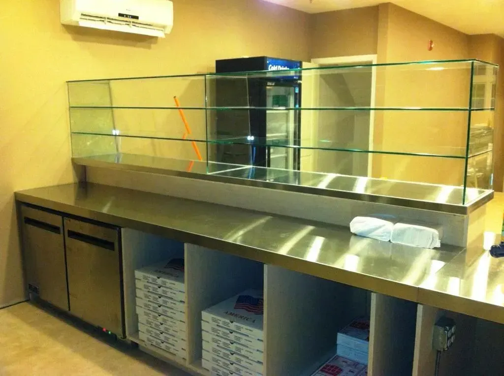 Empty salad bar counter with glass sneeze guard and metal countertop in a cafeteria