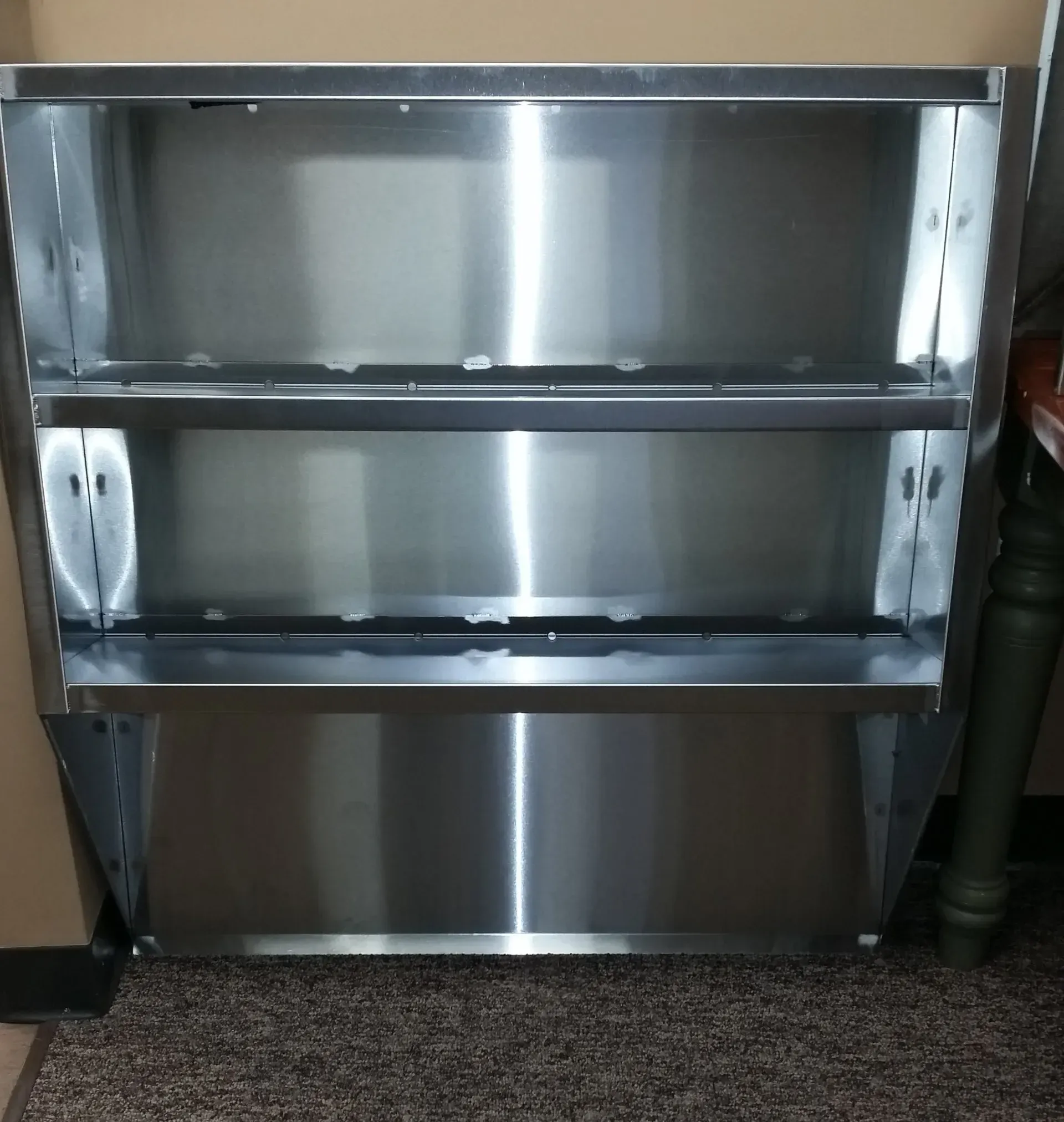 Stainless steel shelving unit with three shelves against a wall in a utility room