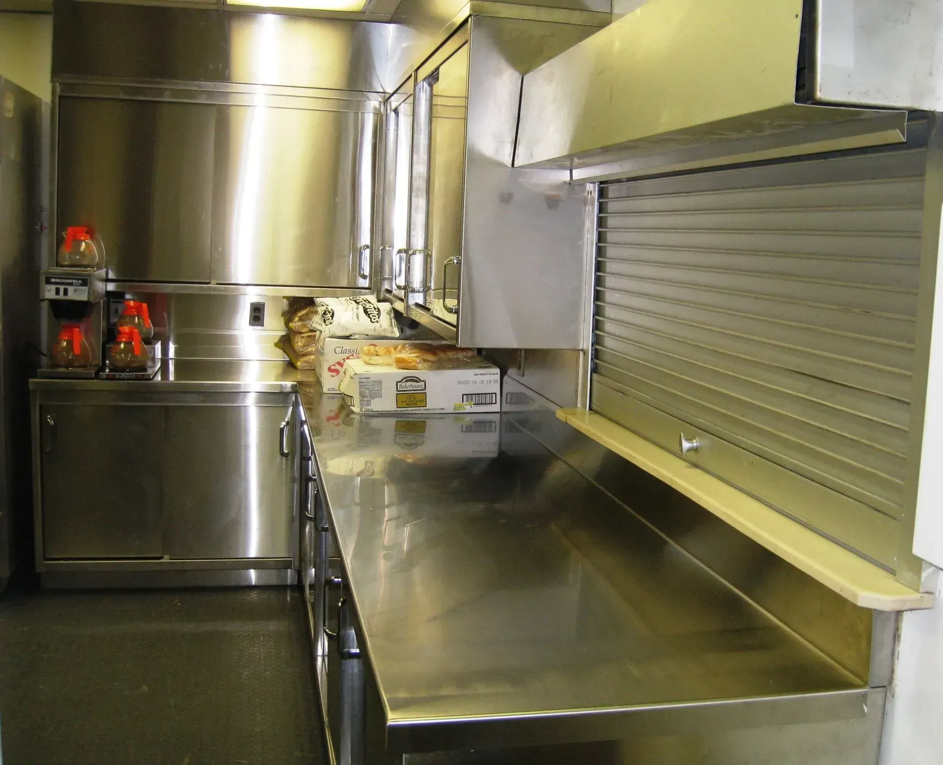 Stainless steel commercial kitchen with counters, large equipment, and a roll-up service window