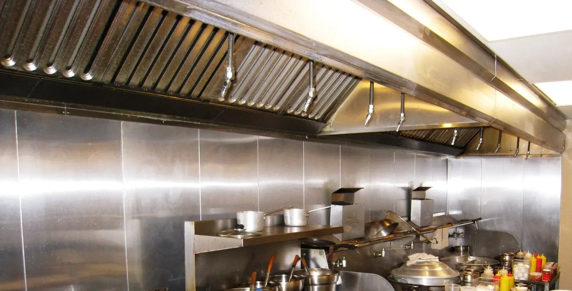 Stainless steel commercial kitchen with range hoods, counters, and cooking pots under bright lights