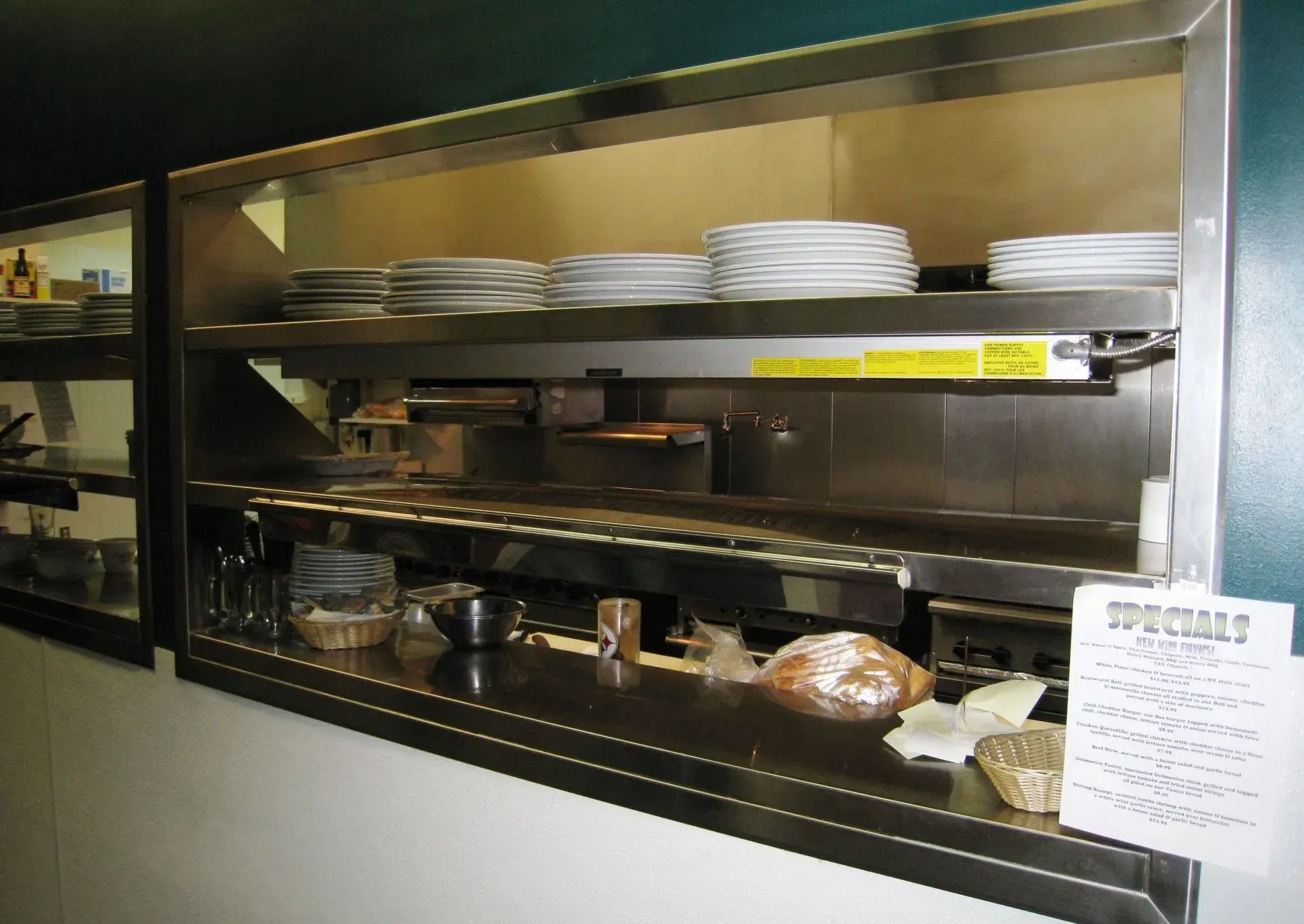Restaurant buffet shelf with stacked plates, serving dishes, and covered food trays under warm lights