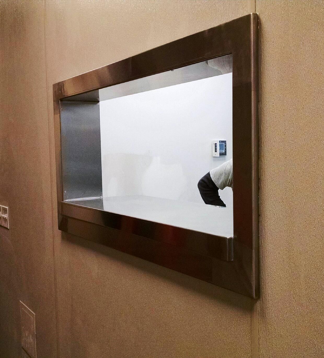 A wall-mounted pass-through window with a stainless steel tray and a white interior counter