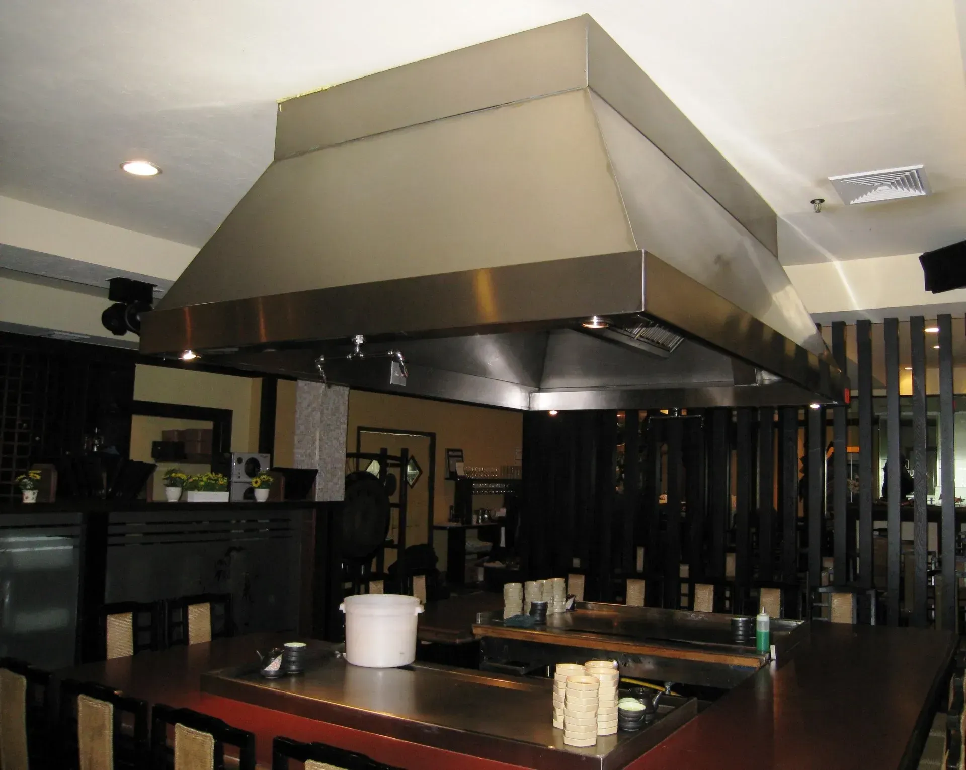 Restaurant interior with a large stainless steel range hood over wooden tables and chairs