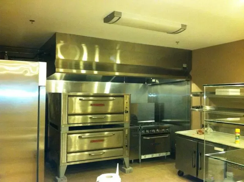 Commercial kitchen with stainless steel ovens, stove, and metal counters under a ventilation hood