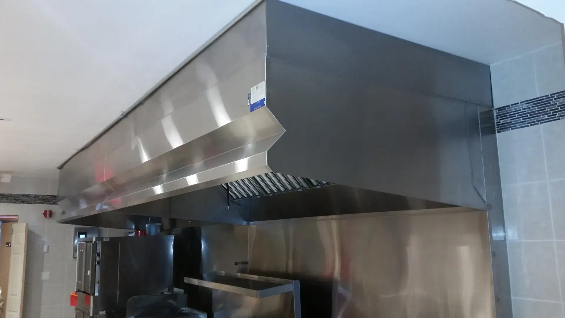 Stainless steel commercial kitchen range hood and ventilation system above cooking equipment