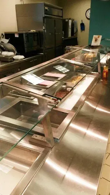 Restaurant buffet counter with glass sneeze guard, stainless steel trays, and kitchen equipment in the background