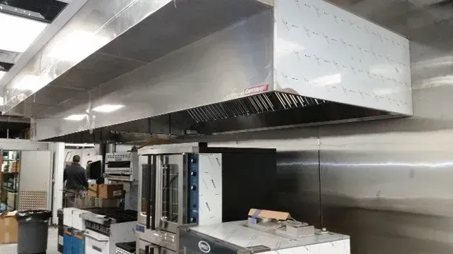 Commercial kitchen with stainless steel ventilation hoods over cooking equipment and prep counters.