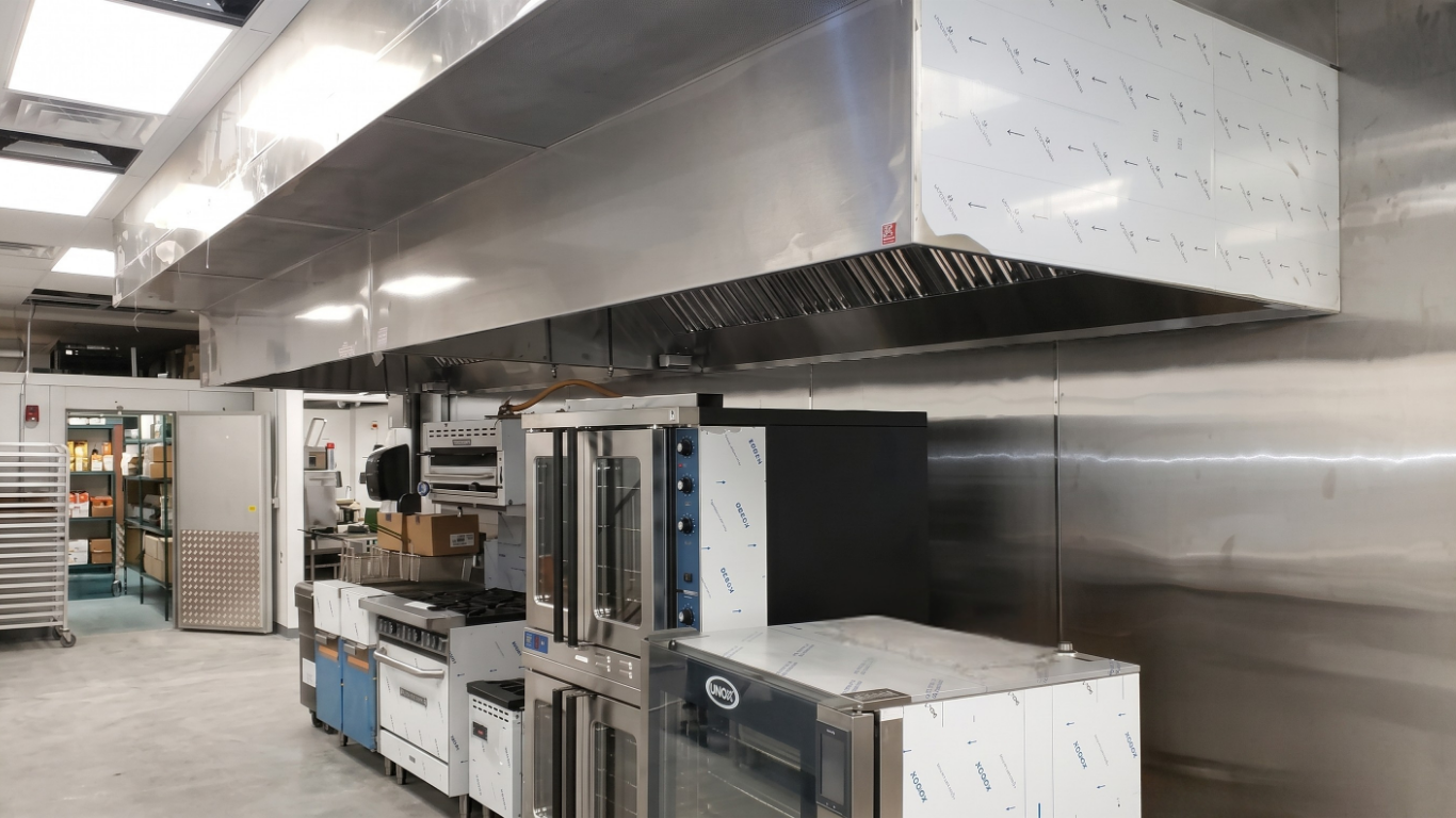 Large copper kitchen hood above a stainless-steel cooking area with two people below it