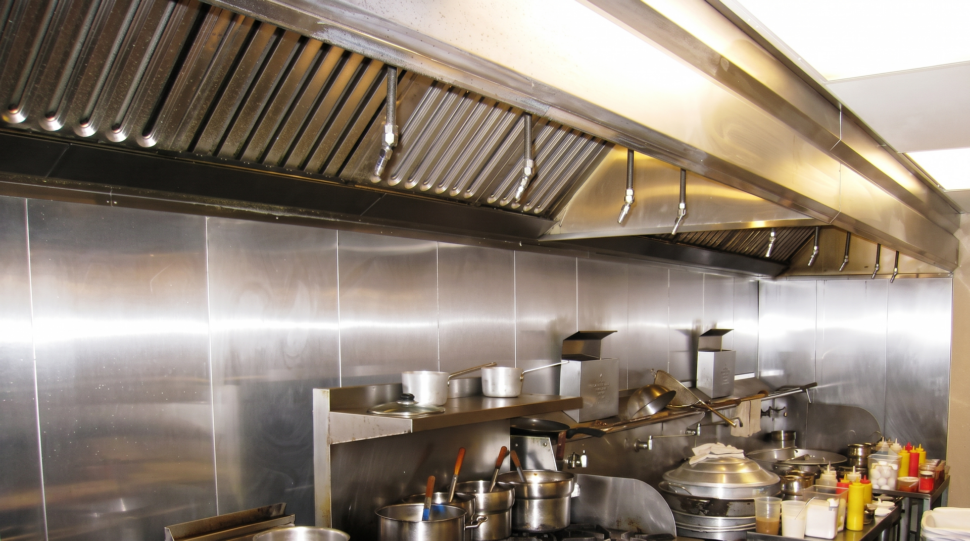 Commercial kitchen with stainless steel counters, stoves, and ventilation hood in a warm-lit restaurant prep area