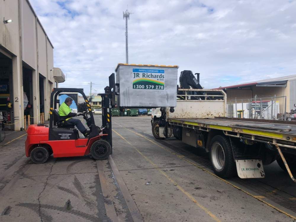 A Man Is Driving a Forklift Next to A Truck — AAA Equipment Pty Ltd In Kempsey, NSW