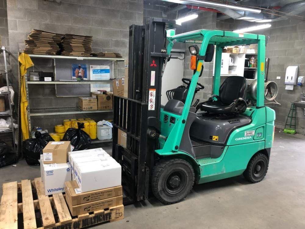 A Green Forklift Is Parked in A Room Filled with Boxes and Pallets — AAA Equipment Pty Ltd In Kempsey, NSW