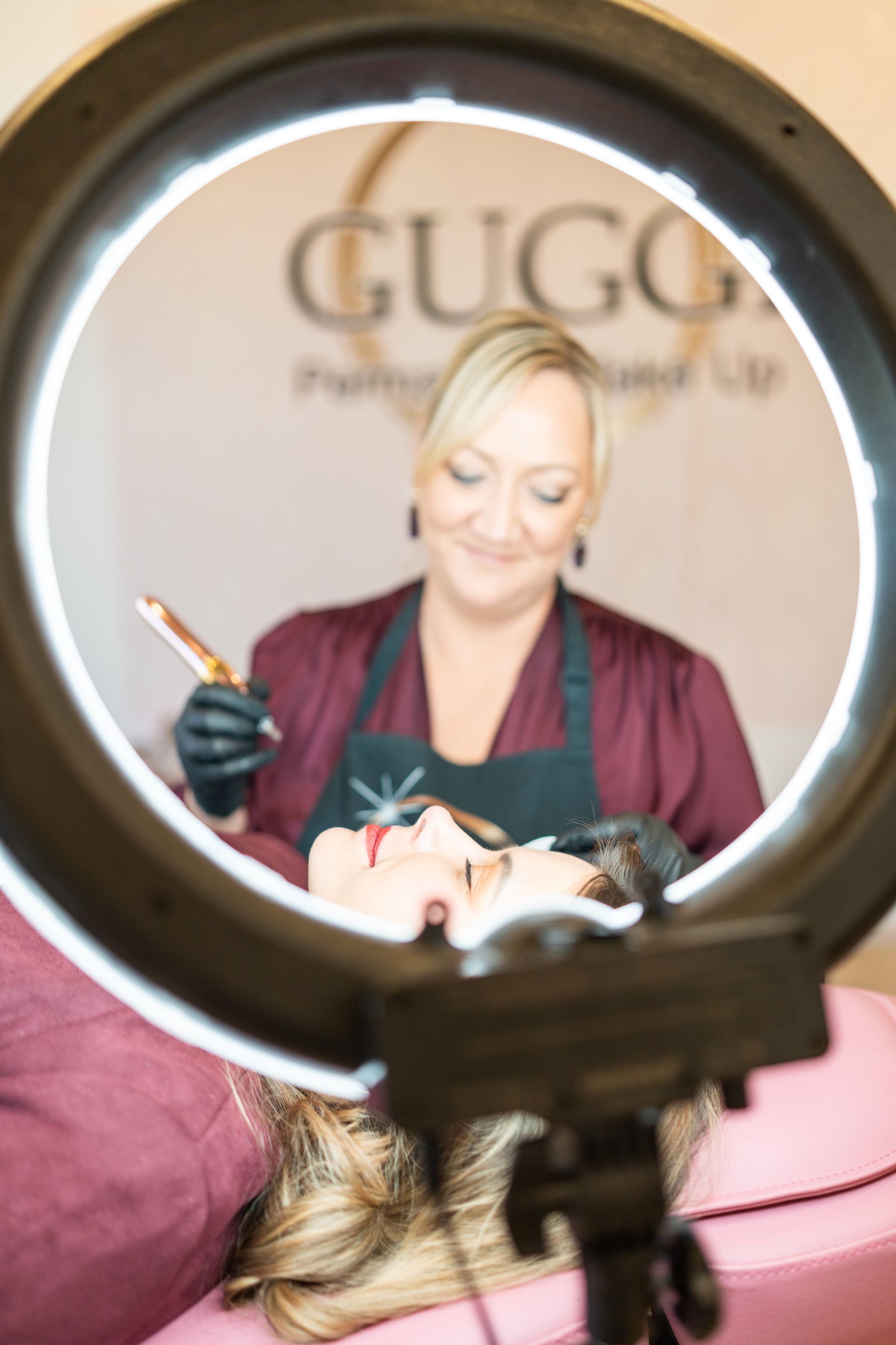 Frau führt kosmetische Behandlung durch, Kundin liegt. Helles Ringlicht.