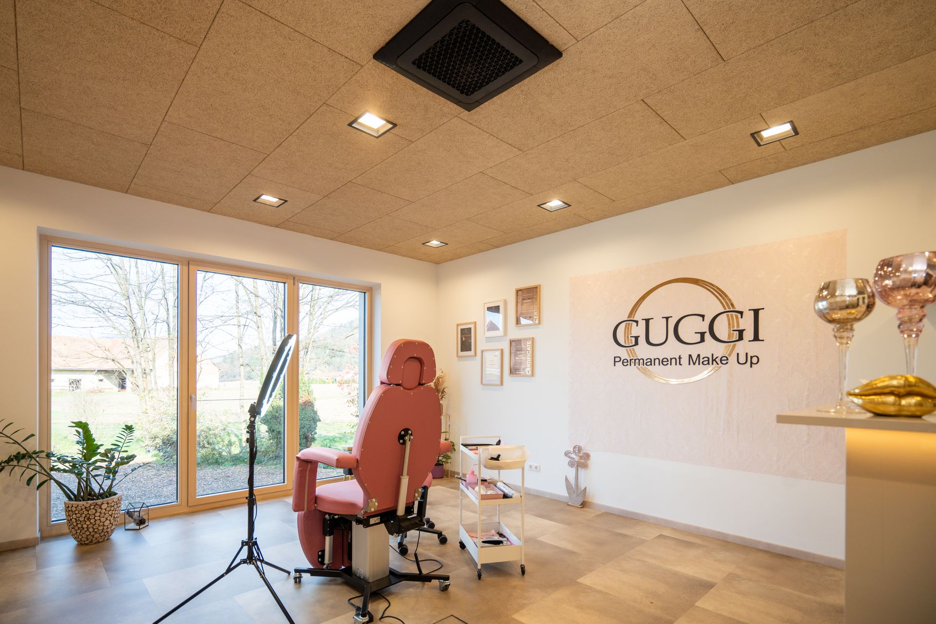 Interieur eines Schönheitssalons mit einem rosa Stuhl, einem großen Fenster und dem Logo „GUGGI“.