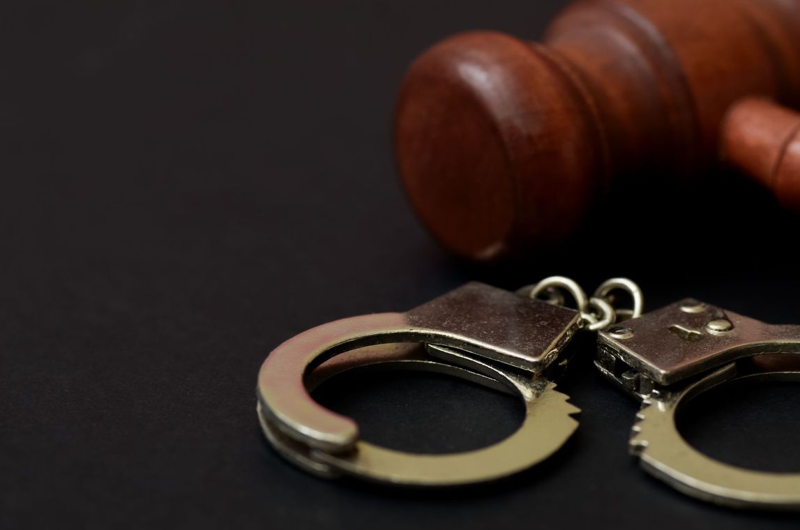 Handcuffs beside a wooden gavel on a dark surface