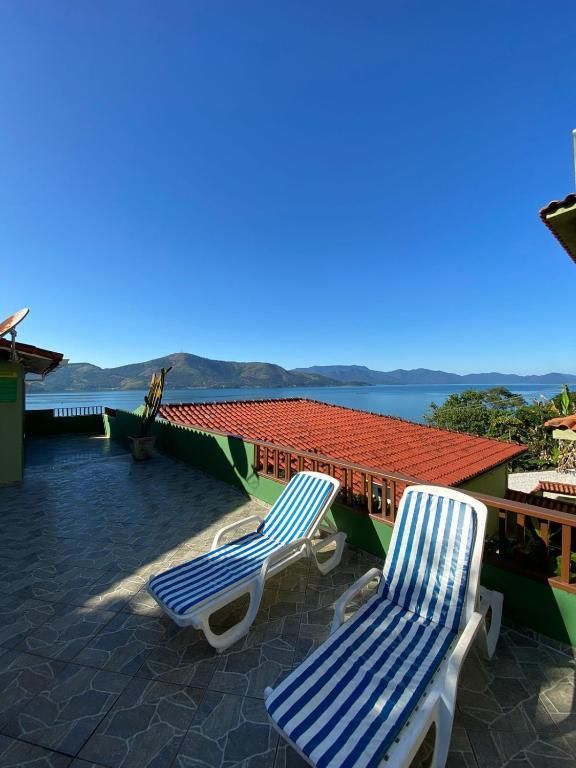 Duas espreguiçadeiras listradas em um deck de azulejos com vista para uma baía com montanhas e um céu azul límpido.