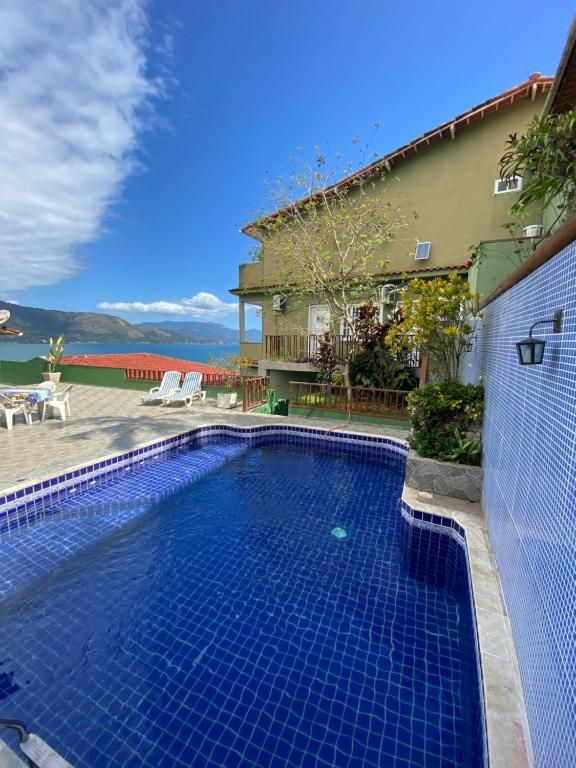 Piscina em frente a um prédio verde com céu azul e vista para o mar.