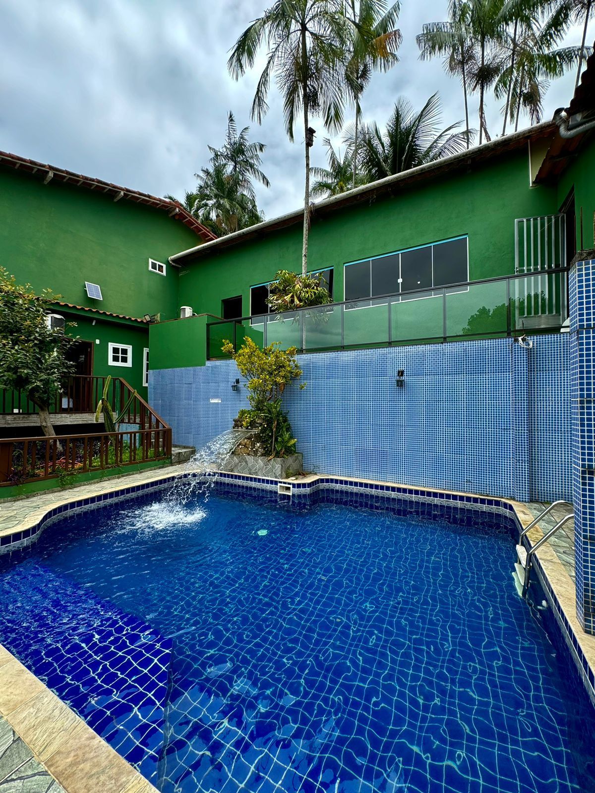 Piscina com cascata em frente a um edifício verde com palmeiras por cima.