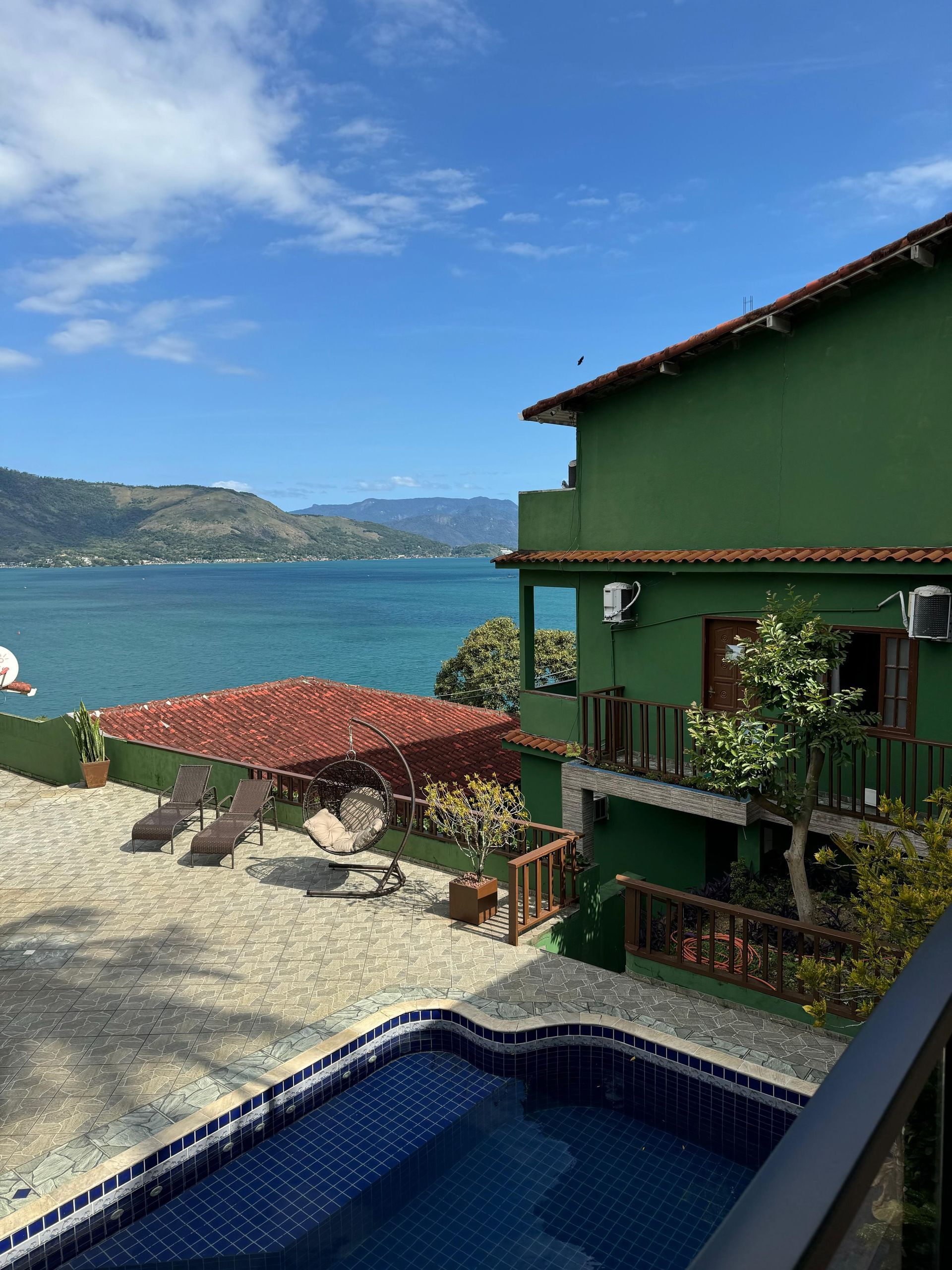 Estufa com piscina e vista para uma baía sob um céu azul.
