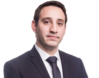 A man in a suit and tie is standing in front of a white background.